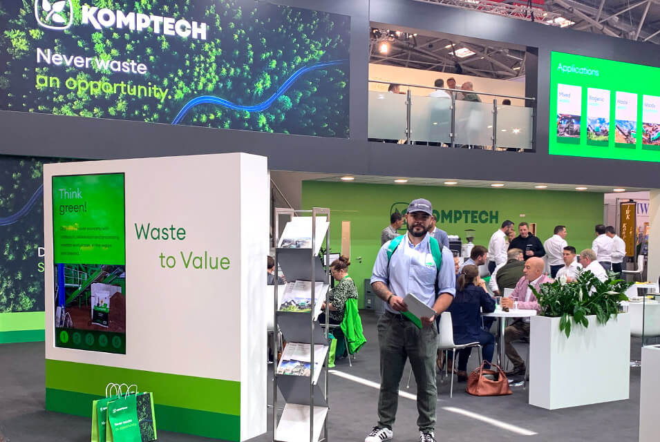 Colaborador de GRÜN Engineering presente en el stand verde, blanco y gris, de la marca Komptech, desarrolladores de máquinas para el reciclaje de residuos, dentro de la IFAT 2022