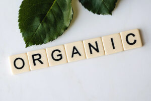 Palabra "Organic" formado con fichas de Scrabble, sobre fondo blanco junto a hojas de plantas