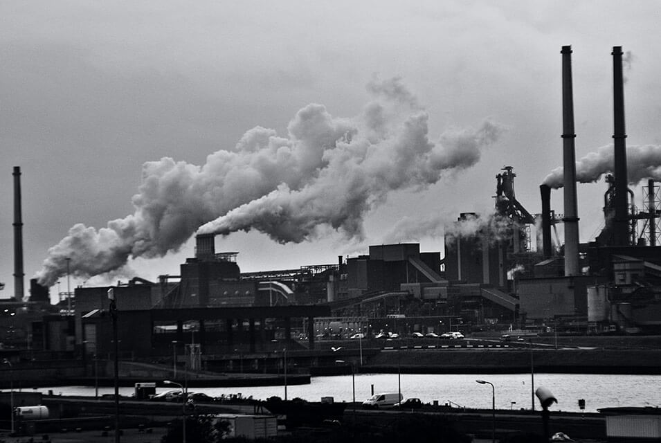 Fumarolas saliendo por chimeneas de fábrica, haciendo referencia a las energías fósiles que son perjudiciales para el medio ambiente